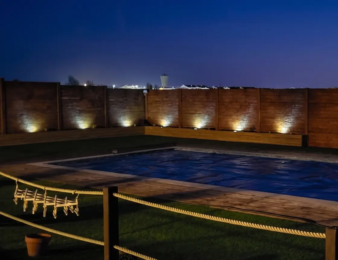 Muro pré-fabricado em betão com iluminação rasante junto a uma piscina, ao anoitecer